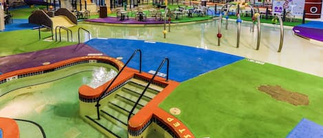 Un parque acuático interior con varias piscinas, toboganes y estructuras de juego.