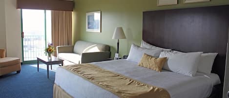 Quarto de hotel com uma cama grande, um sofá, uma mesinha com um vaso e vista para o exterior.