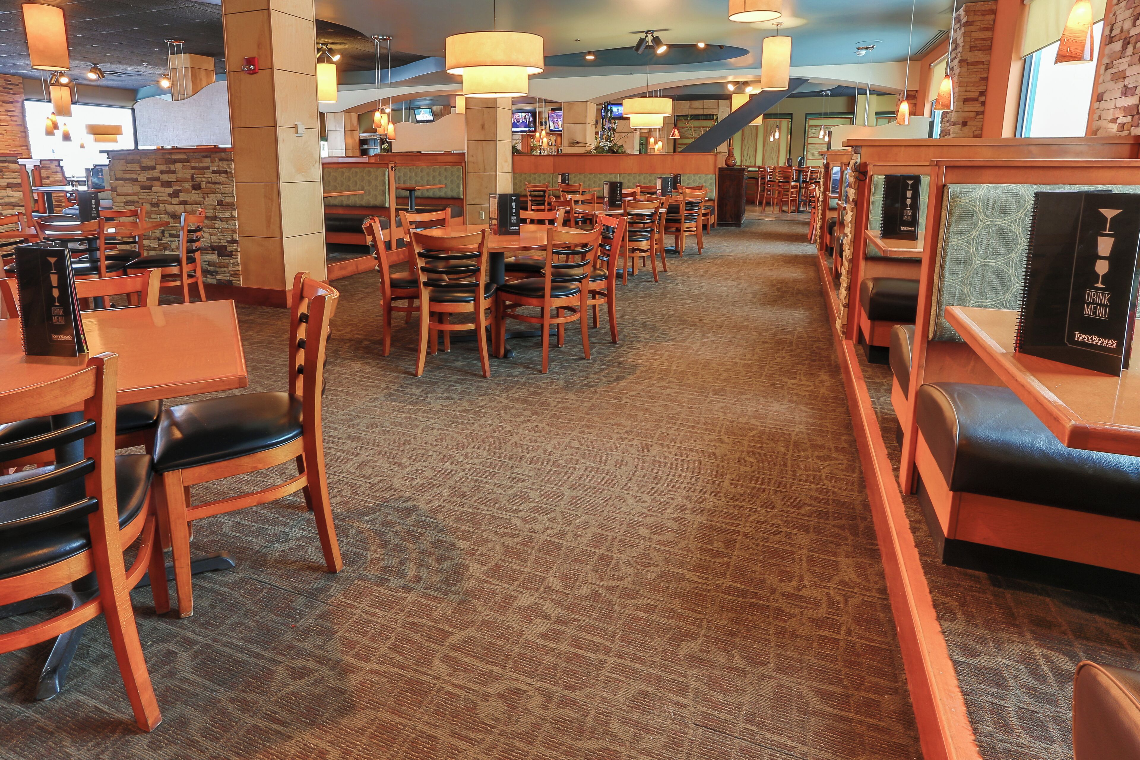 Un restaurante con mesas y sillas de madera, suelo alfombrado y lámparas colgantes.