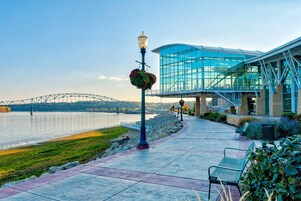 Un paseo marítimo con un edificio de vidrio, un puente al fondo y un farol adornado con flores.