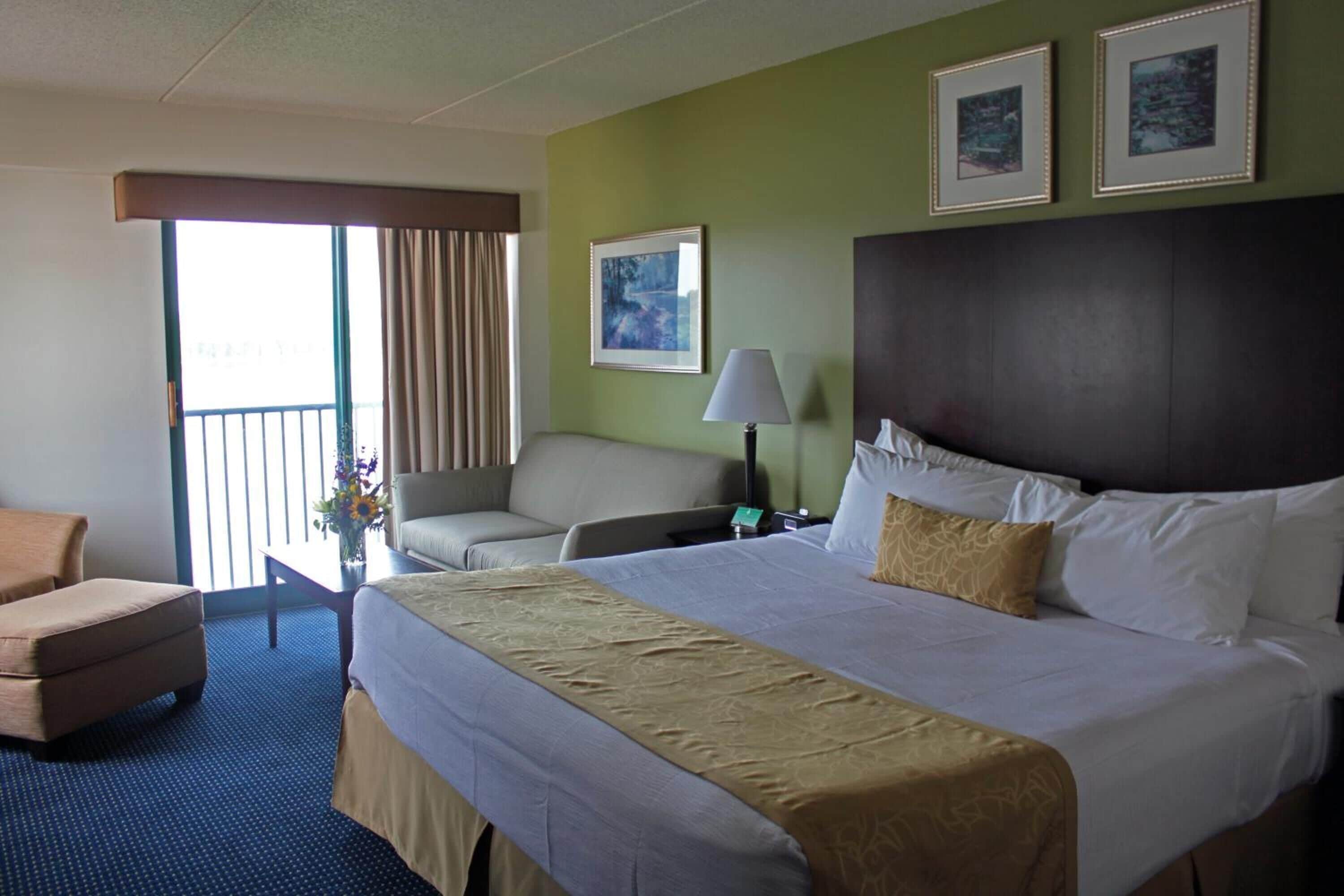 A hotel room with a large bed, a sofa, a desk, and a view of the outdoors.