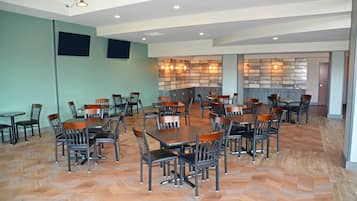 A spacious dining area with multiple tables and chairs, a herringbone floor pattern, and a wall with a built-in light fixture.