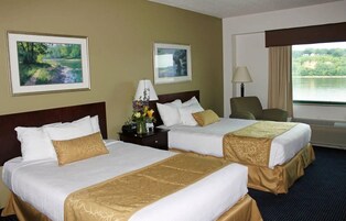 Habitación de hotel con dos camas, una mesita de noche con lámpara, una silla y dos cuadros en la pared.
