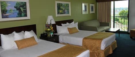A hotel room with two beds, a desk, a chair, and a balcony with a view.