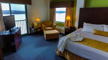 Una habitación de hotel con cama, una silla, un escritorio con televisor y vista a un cuerpo de agua.