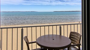 Un balcone con tavolo e sedie affacciato su una spiaggia e un mare calmo.
