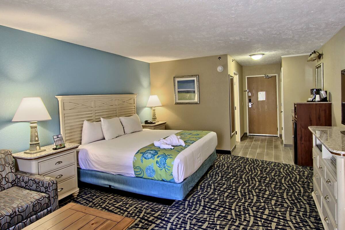 A hotel room with a bed, two bedside tables with lamps, a chair, a dresser, and a patterned rug.