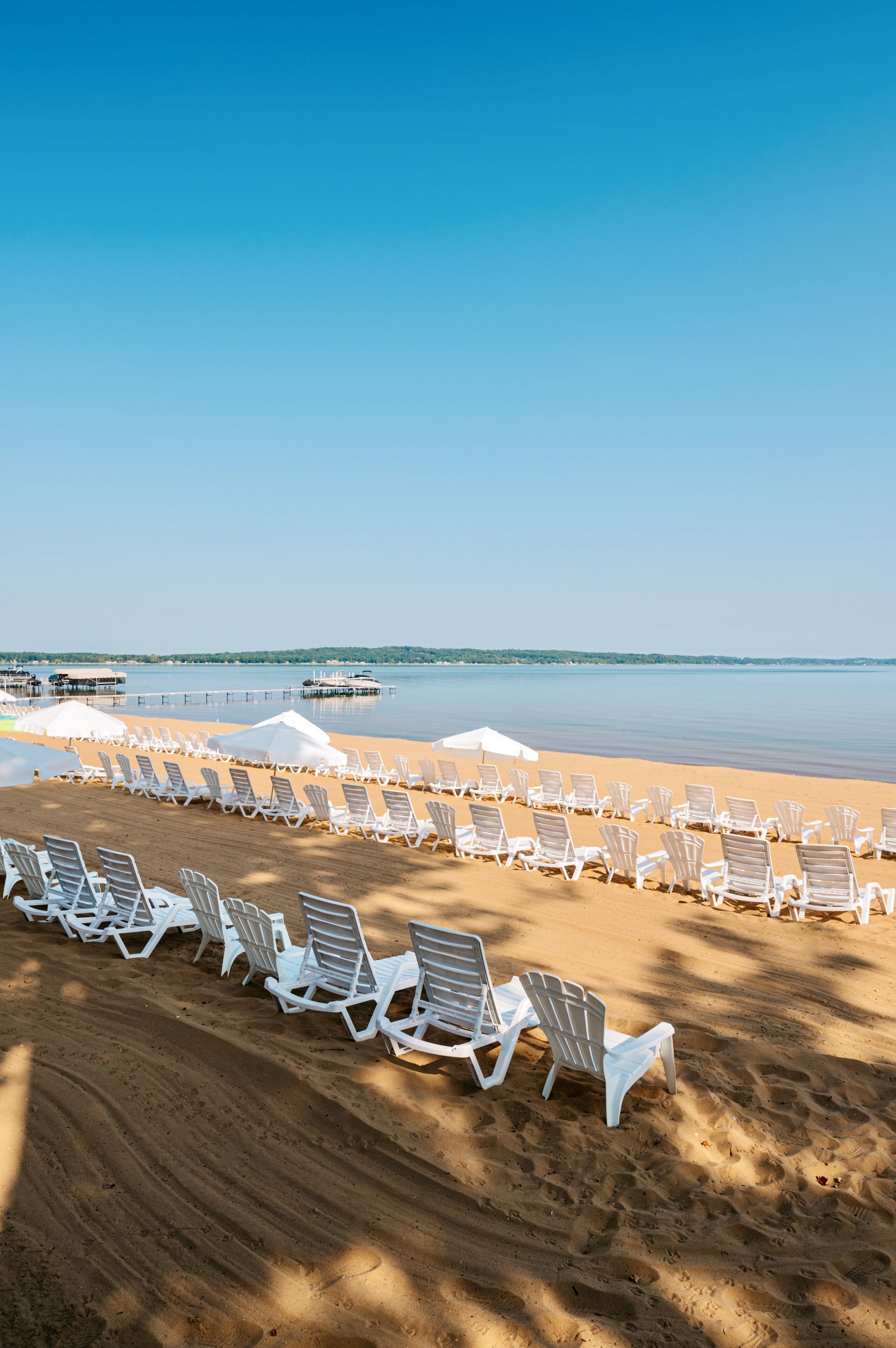 Una spiaggia con file di sedie a sdraio bianche e ombrelloni, cielo sereno e acqua calma.