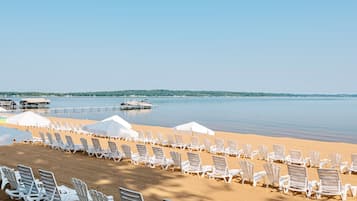 Una spiaggia con file di sedie a sdraio bianche e ombrelloni, cielo sereno e acqua calma.