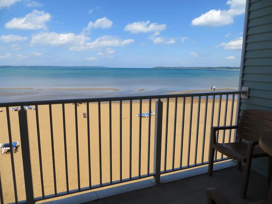 A balcony with a view of a beach, a railing, and a chair.