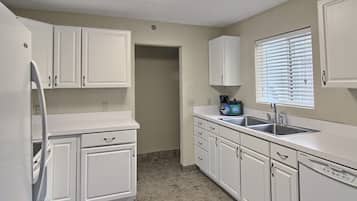 A kitchen with white cabinets, a sink, and a window with blinds.