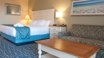 A hotel room with a bed, a bedside table with a lamp, a chair, a small table, and a painting on the wall.