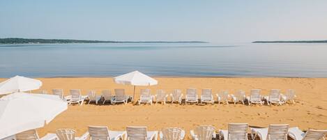 A beach with rows of white lounge chairs and umbrellas.