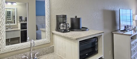 Et badeværelse på et hotel med vask, spejl, kaffemaskine, mikroovn og et skab med skuffer.