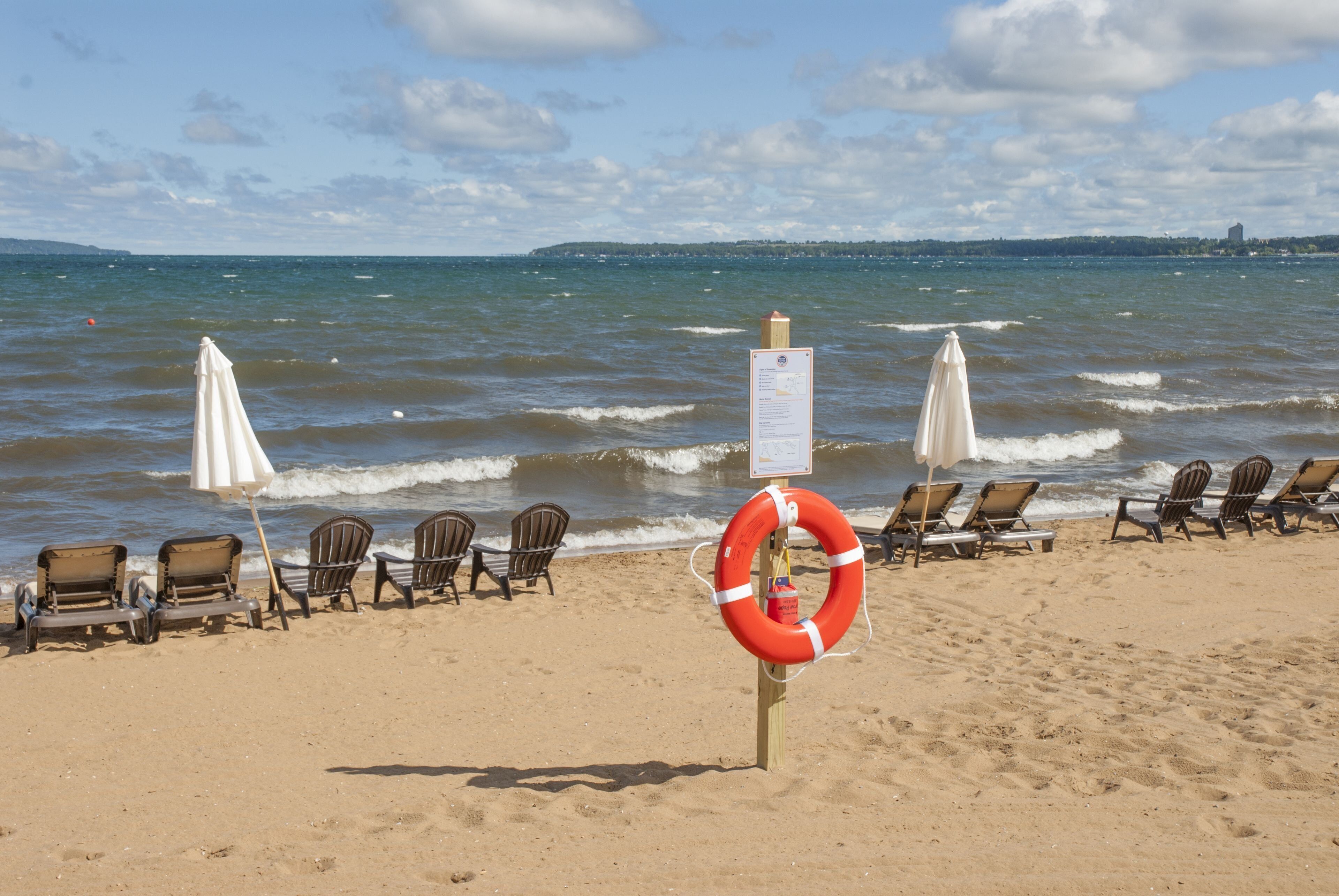 Une plage bordée de rangées de chaises de plage et de parasols, une bouée de sauvetage et un panneau indicateur.