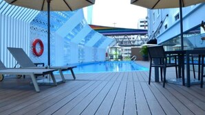 Ein Poolbereich mit Liegestühlen und Sonnenschirmen, umgeben von einer weißen Mauer mit Löchern und einem Rettungsring.