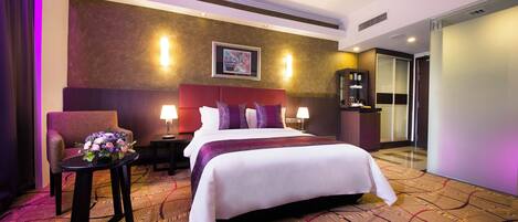 Ein Hotelzimmer mit einem großen Bett, einem Sessel, einem kleinen Tisch mit Blumenvase und einem Nachttisch.