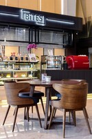 A café with a modern interior, featuring a counter with a red espresso machine, a display of pastries, and wooden chairs around a table.