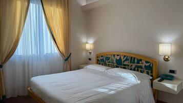 Ein Hotelzimmer mit einem großen Bett, zwei Nachttischen mit Lampen, einem Fenster mit Vorhängen und einem Blumenmuster an der Kopfteile.