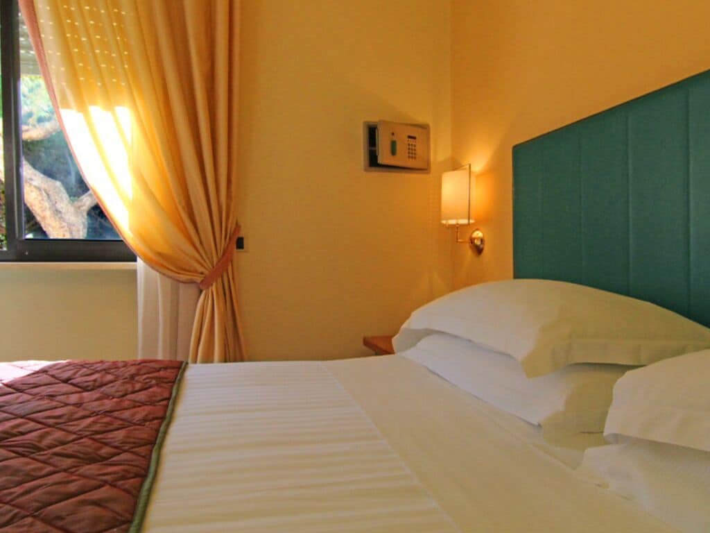 Een hotelkamer met een bed, een thermostaat aan de muur en een raam met gordijnen.