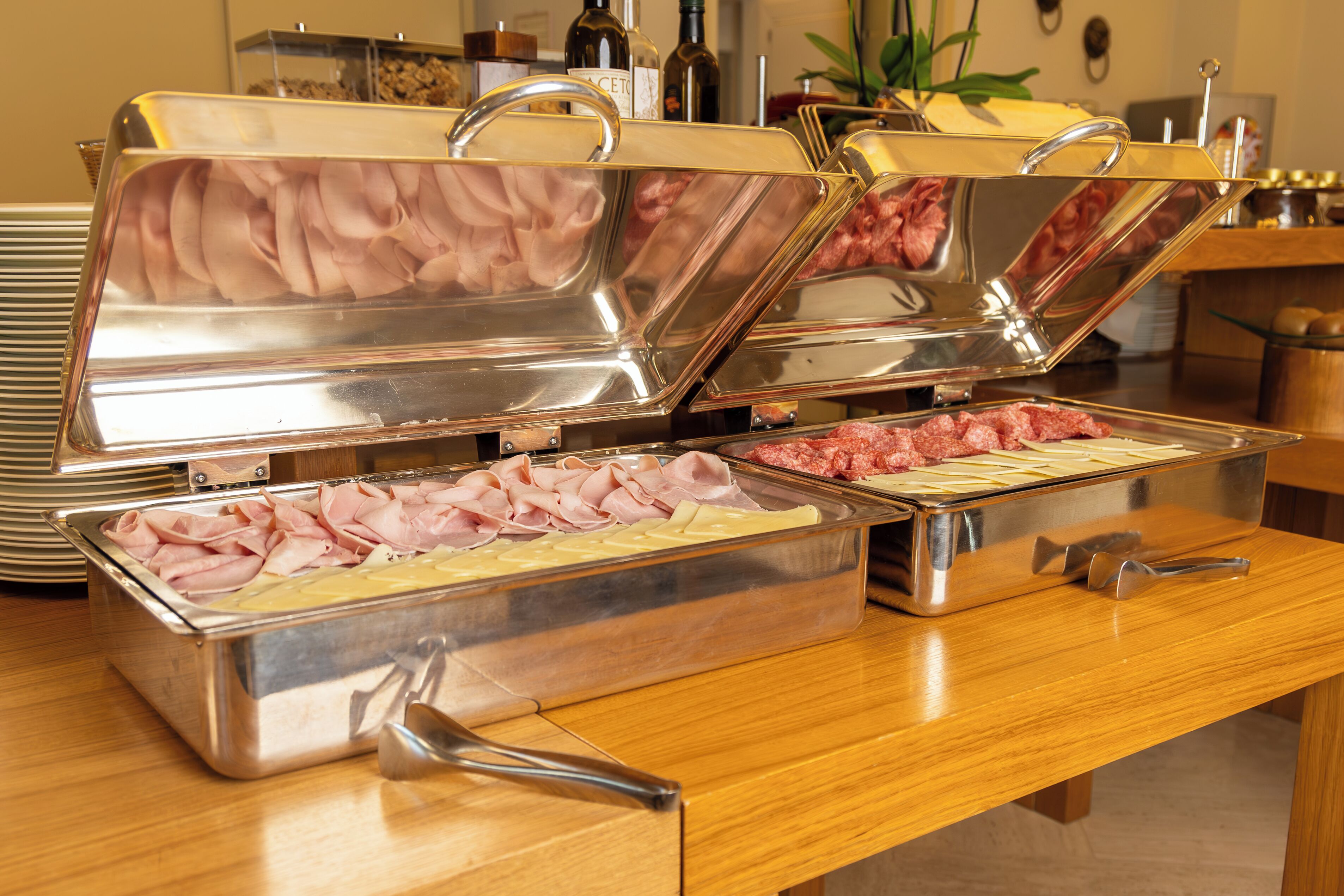 A buffet with multiple stainless steel chafing dishes containing various meats and cheeses.