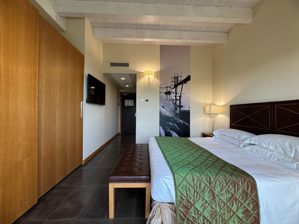 A hotel room with a bed, a bench, a wardrobe, and a wall-mounted TV.