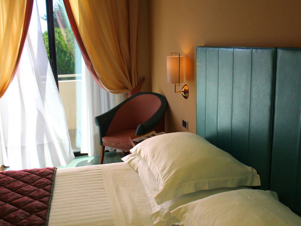 Una habitación de hotel con una cama, una silla, una lámpara en la pared y una ventana con cortinas.