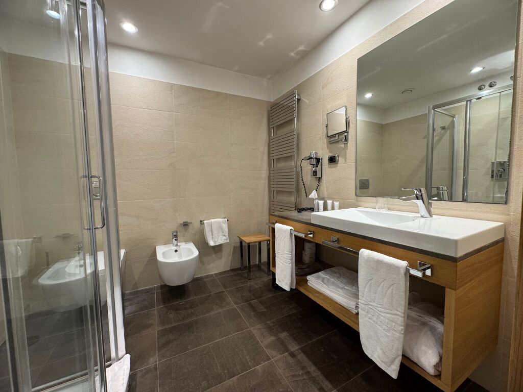 Une salle de bain moderne dotée d’une douche à parois de verre, d’un bidet, d’un meuble-lavabo avec un grand miroir et d’un meuble en bois.