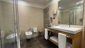 Un baño moderno con cabina de ducha de vidrio, un bidé, un tocador con un espejo grande y un mueble de madera.
