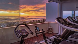 A balcony with a treadmill and a stationary bike, overlooking a sunset over the ocean. - Hotel Cristallo (Giulianova)