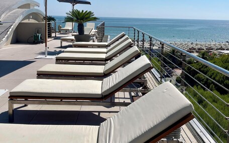 A rooftop terrace with sun loungers and umbrellas overlooking a beach.