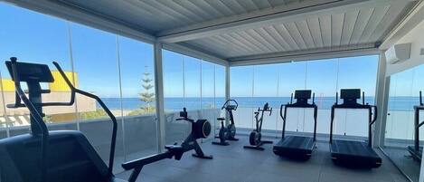 Une salle de sport équipée de divers appareils et offrant une vue sur l’océan.