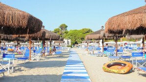 A beach with rows of blue lounge chairs and thatched umbrellas, a lifeguard float, and a clear sky. - Hotel Cristallo (Giulianova)