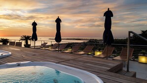 A wooden deck with lounge chairs and umbrellas overlooking a body of water during sunset. - Hotel Cristallo (Giulianova)
