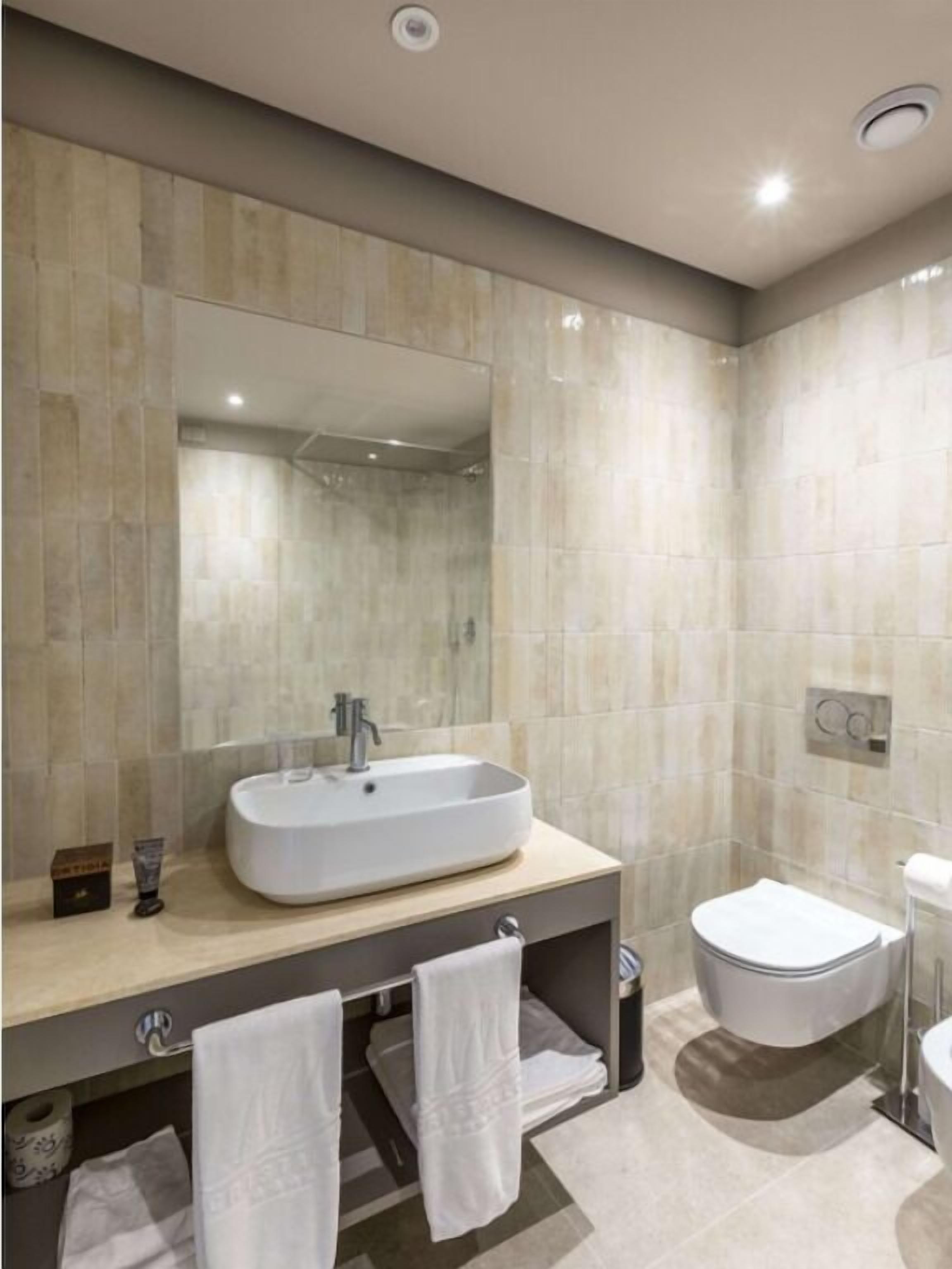 A modern bathroom with a large mirror, a vessel sink, a toilet, and a towel rack.