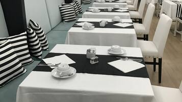 A long dining table with white tablecloths and black placemats, set with plates, cups, and cutlery.