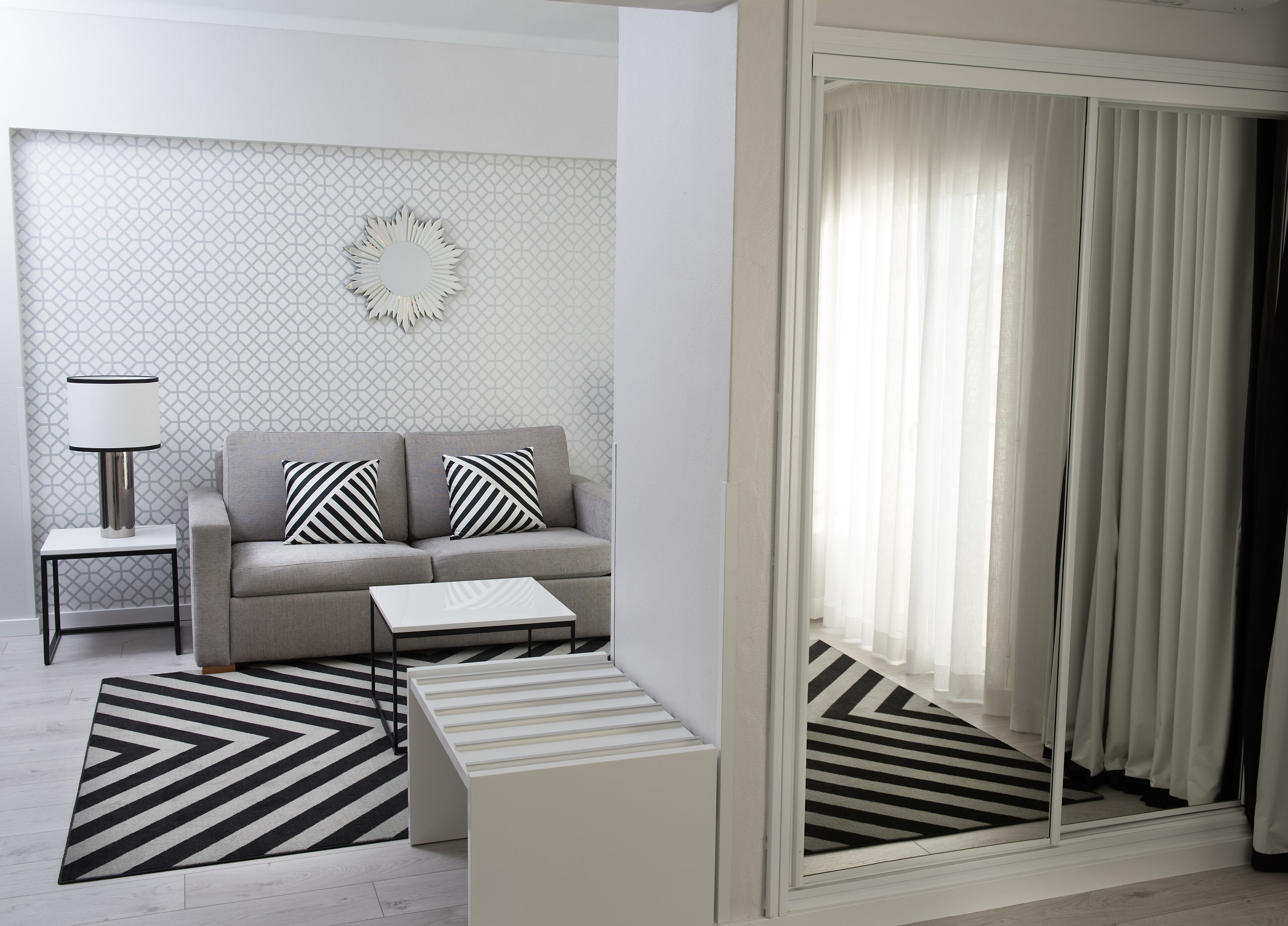 A modern living room with a grey sofa, two striped pillows, a side table with a lamp, a coffee table, and a patterned rug.