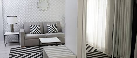 A modern living room with a grey sofa, two striped pillows, a side table with a lamp, a coffee table, and a patterned rug.