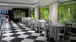 A restaurant with a checkered floor, white tables, and chairs, large windows with a view of greenery. - Hotel Cristal Marinha (Marinha Grande)
