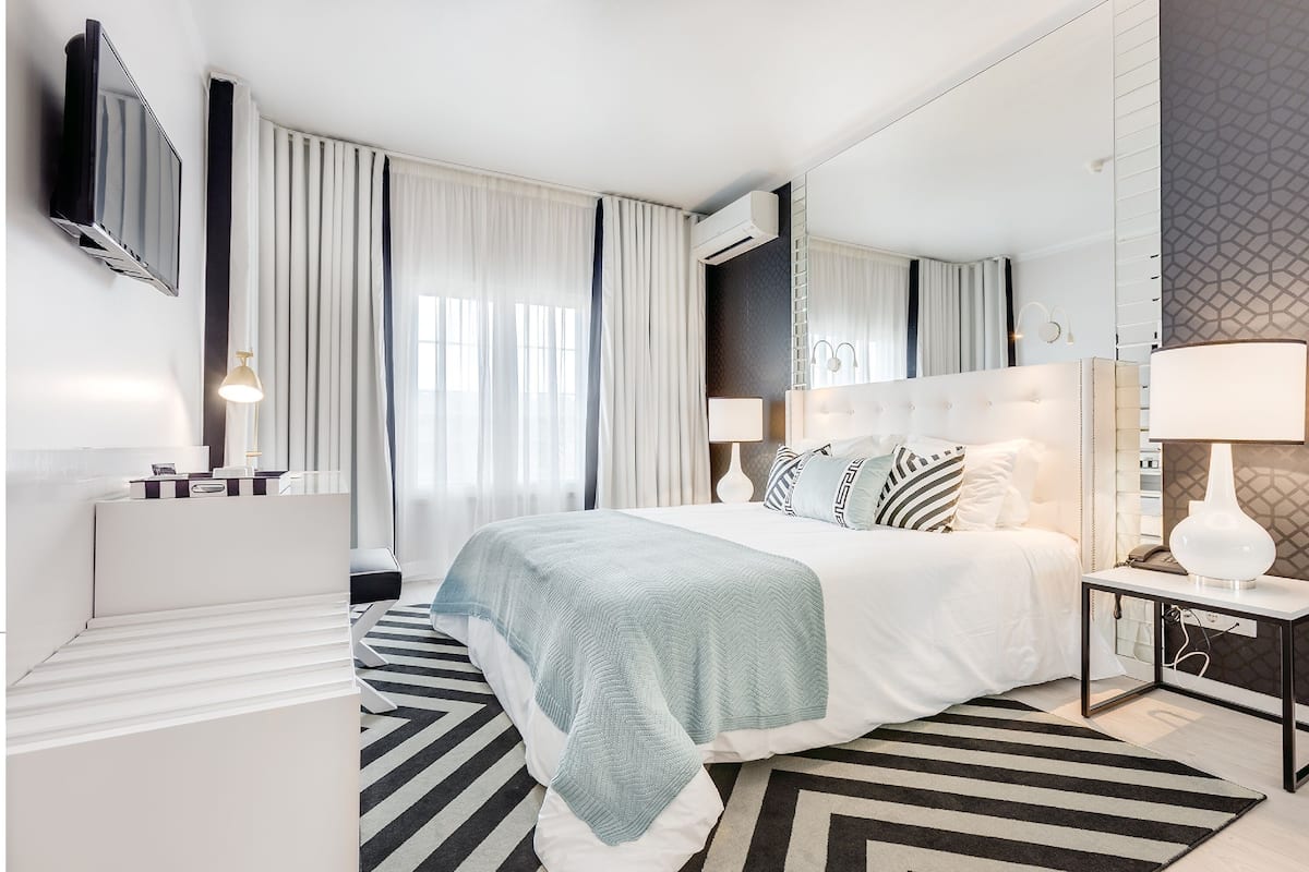 Una habitación de hotel moderna con una cama grande, un televisor de pantalla plana, un equipo de aire acondicionado y una mesita de noche con lámpara.