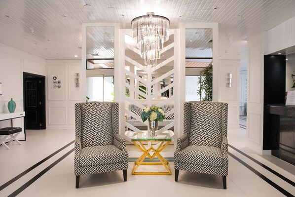 Un lobby moderno con dos sillones estampados, una mesa de centro de cristal y una araña.