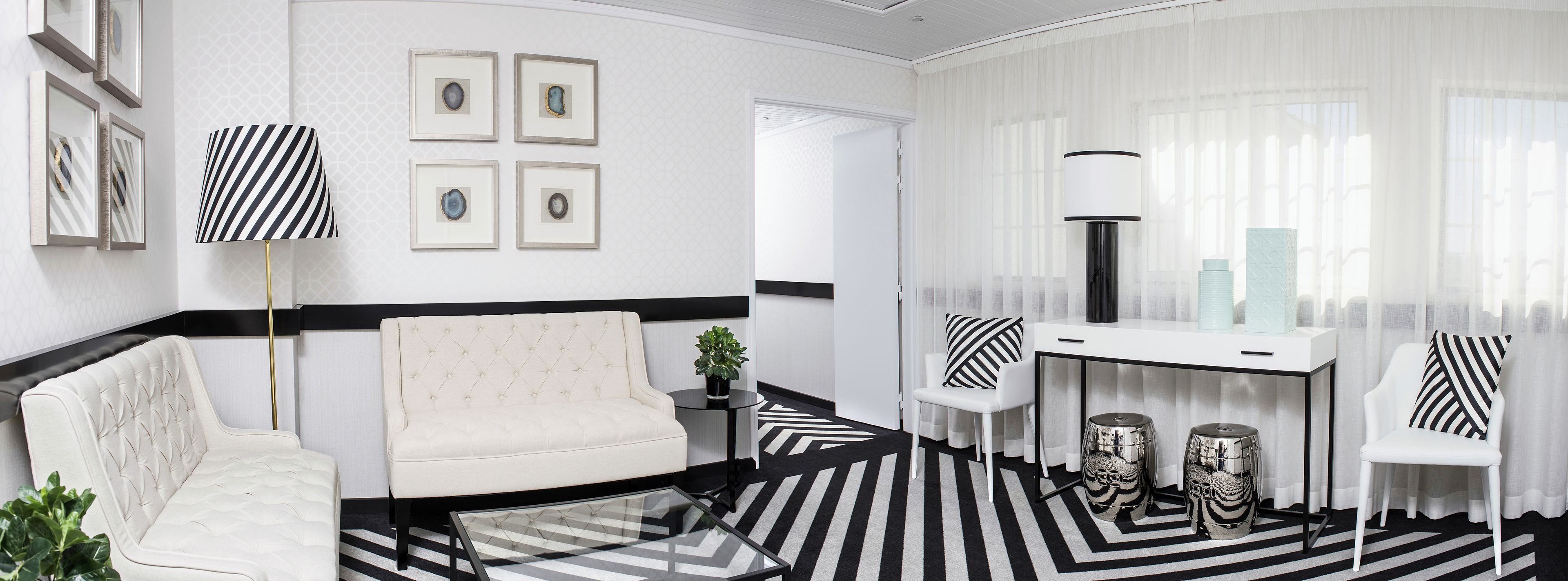 Un salon moderne avec un canapé blanc, une table basse en verre, une table d’appoint blanche agrémentée d’une plante, un lampadaire à rayures et un fauteuil blanc avec un coussin à rayures.