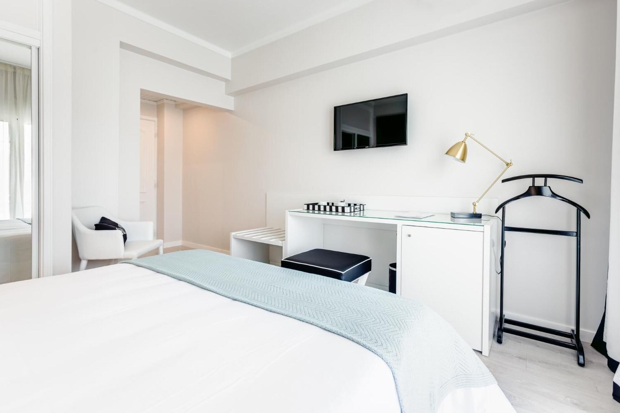 A modern hotel room with a large bed, a desk with a computer, a TV, and a desk lamp.