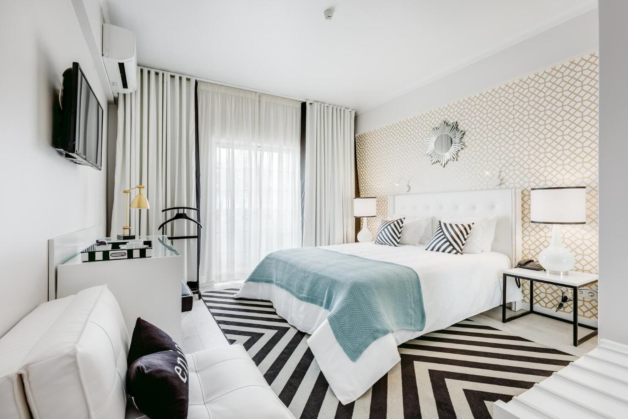 A modern hotel room with a bed, bedside table, lamp, and a TV mounted on the wall.