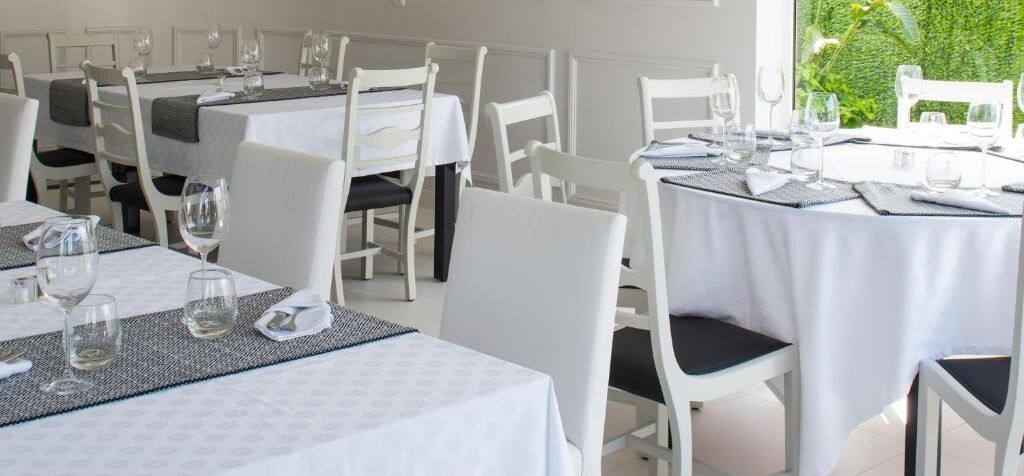 A restaurant with white tables and chairs, each set with wine glasses and cutlery.