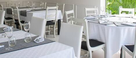 Un restaurante con mesas y sillas blancas, cada conjunto con copas de vino y cubiertos.