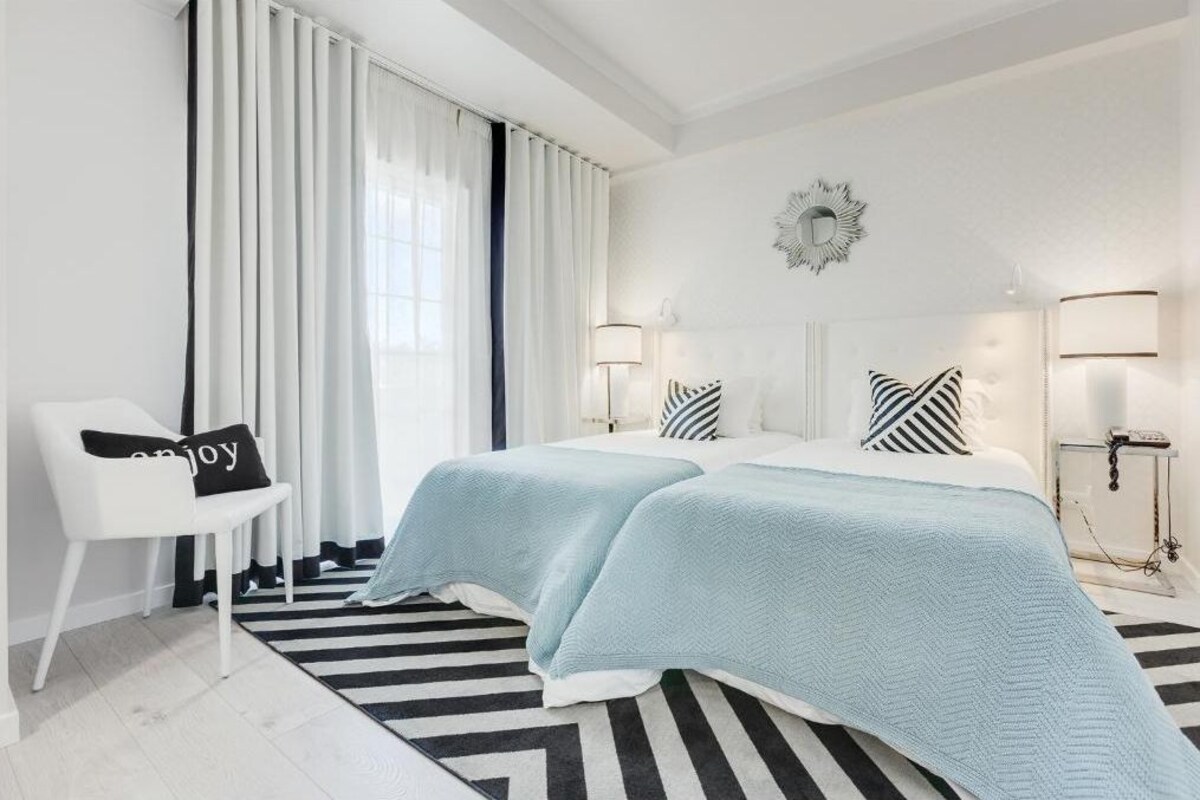 Habitación de hotel con dos camas, una silla, un alfombra a rayas y un espejo grande en la pared.