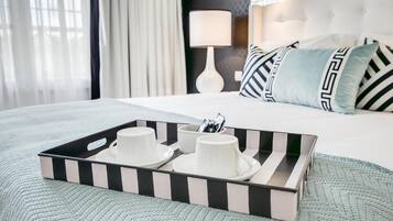 A neatly made bed with a tray of white cups and saucers, a lamp, and patterned pillows.