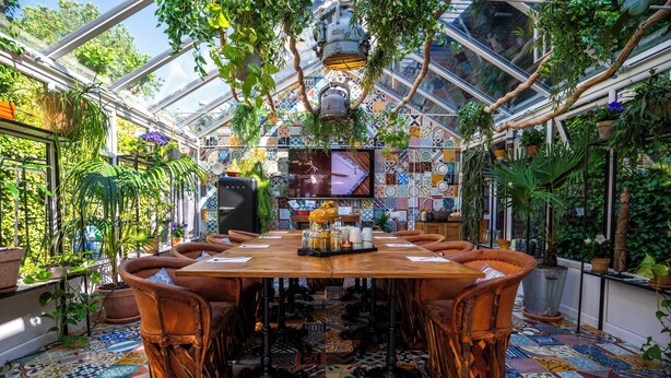 Une pièce de style serre, avec une grande table et des chaises, entourée de plantes en pot et dotée d  ’un sol carrelé.