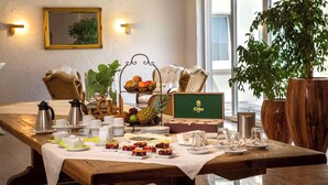 Mesa de café da manhã posta com chá, café, frutas e doces, com vista para o exterior.